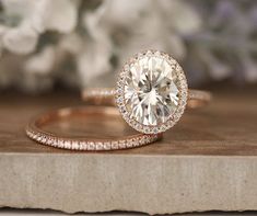 an engagement ring and wedding band on top of a wooden table with flowers in the background