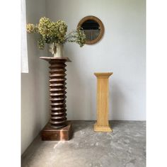 a vase with flowers sitting next to a tall wooden object on the floor in front of a mirror