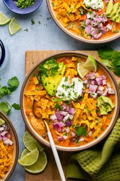 two bowls filled with chicken tortilla soup on top of a wooden cutting board