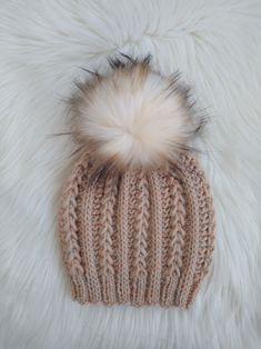 a knitted hat with a fur pom on top sitting on a fluffy white blanket