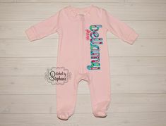 This listing is for one monogrammed light pink footed baby sleeper. Available sizes are NB, 3m, 6m, 9m, 12m, 18m, 2T, and 3T. Your child's name is appliqued with turquoise thread using a colorful floral fabric. A middle name can be added underneath if desired. All my items are rinsed in water and tumble dried to prevent shrinking once the embroidery is added. Sleepers are also available in white, red, grey, navy, and light blue. When you place your order, please let me know what color sleeper yo Pink Long Sleeve Footie For Bedtime, Pink Onesie For Bedtime In Spring, Pink Onesie For Bedtime And Spring, Fitted Pink Onesie For Bedtime, Fitted Pink Onesie For Loungewear, Fitted Pink Onesie With Name Print, Pink Fitted Onesie With Name Print, Cute Pink Onesie With Name Print, Personalized Fitted Pink Onesie