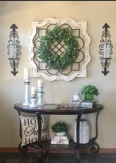 a table with some plants on top of it next to a wall mounted wreath and candles