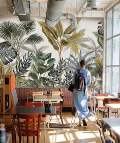 a woman walking in front of a wall mural with tropical leaves and plants on it