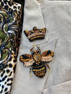 two bee brooches sitting on top of a white shirt next to a leopard print tie