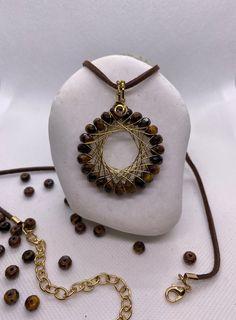 This absolutely unique, handmade necklace features semiprecious Tiger's Eye gemstone faucet beads wrapped in a gold-tone brass wire.  The diameter of the pendant is approximately 4cm (1.5 inches). The length of suede cord is 45cm (17.7inches) and 55 (21.6inches) with extension chain.  The color of the cord is brown. Black and beige cords are also available. Comfortable to wear. Made to last. Shipped in a gift box. Adjustable Hand Wrapped Gold Beaded Necklaces, Wire Wrapped Round Pendant Amulet Jewelry, Wire Wrapped Round Pendant Amulet, Gold Wire-wrapped Pendant Crystal Necklaces, Gold Wire-wrapped Pendant Crystal Necklace, Wire Pendant Necklace As A Gift, Gold Wire-wrapped Crystal Pendant Necklace, Wire Pendant Necklace For Gift, Gold Wire Wrapped Crystal Pendant Necklace