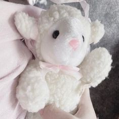 a white teddy bear with a pink bow on its head sitting in someone's lap