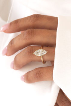 a woman's hand wearing a gold ring with an oval shaped diamond on it