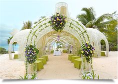 an outdoor wedding setup on the beach with flowers and greenery in front of it