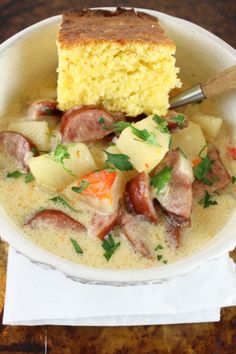 a white bowl filled with cornbread and ham soup next to a piece of bread