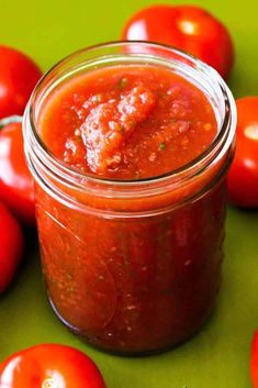 a glass jar filled with tomato sauce next to some red tomatoes on a green surface