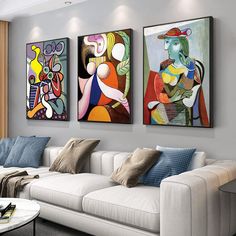 three paintings hang on the wall above a white couch in a living room with two windows