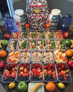 a variety of fruits and vegetables are arranged in plastic containers on a table with water bottles