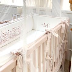 there is a crib with a white sheet on it and pink bows hanging from the rails