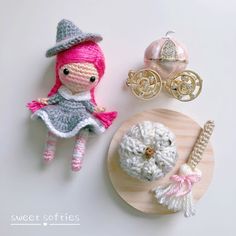 crocheted doll and accessories displayed on white surface next to wooden plate with gold brooch