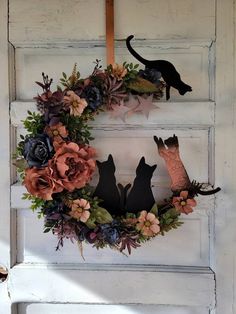 a wreath with two cats and flowers hanging on the front door to make it look like they're coming out of the woods