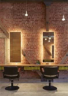 two salon chairs are facing each other in front of a brick wall with lights on it