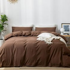 a bed with brown sheets and pillows in a room next to a plant on the floor