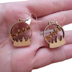 a pair of earrings that are in the palm of someone's hand with trees on it