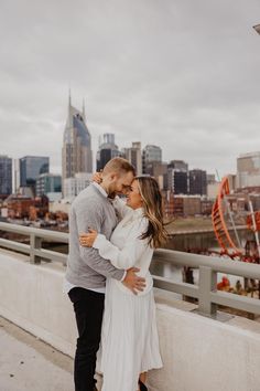 a man and woman standing next to each other on a bridge in front of the city