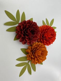 three red and orange paper flowers on a white surface