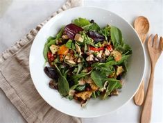 a white bowl filled with salad on top of a table next to wooden utensils