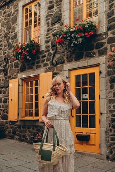 a woman in a white dress carrying a green bag and standing next to a stone building