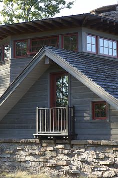 a wooden house with red windows and a deck on the front porch is surrounded by stone walls