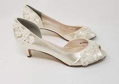 a pair of white wedding shoes with flowers on the heel and lace trimmings