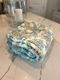 a stack of towels sitting on top of a counter next to a glass vase and candle