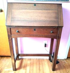 an old wooden desk sitting on top of a hard wood floor next to a pink wall