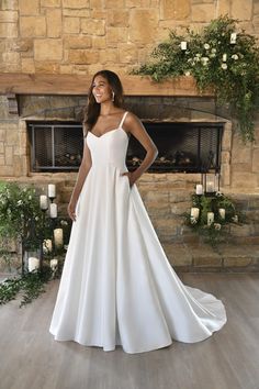 a woman standing in front of a fireplace wearing a white wedding dress with spaghetti straps