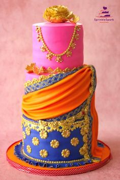 a three tiered cake decorated with gold and pink icing, adorned with an elaborate necklace