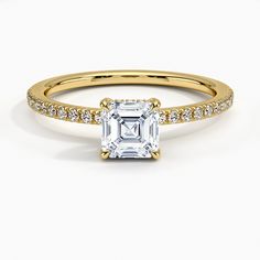 a yellow gold engagement ring with an emerald cut diamond and pave set diamonds on the band