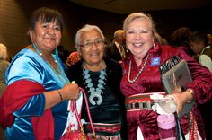 two women standing next to each other holding purses and smiling at the camera while others look on