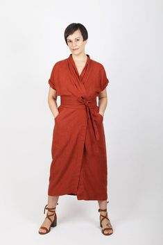 a woman standing in front of a white background wearing a red dress with a knot at the waist