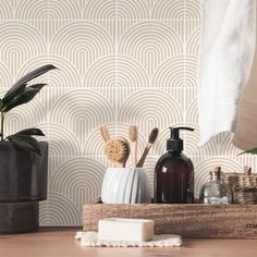 bathroom accessories displayed on wooden table in front of wallpaper with geometric pattern and plant