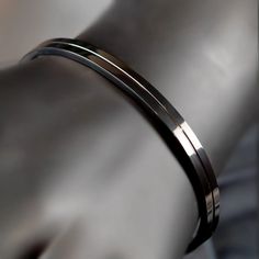 Sleek metallic bracelet or bangle with a polished finish. Modern Black Metal Bangle, Modern Black Stainless Steel Cuff Bracelet, Modern Gunmetal Bracelets For Formal Occasions, Black Stainless Steel Cuff Bracelet, Modern Metal Cuff Bracelet, Black Metal Minimalist Cuff Bracelet, Modern Black Cuff Bangle Bracelet, Modern Black Bracelets, Modern Stainless Steel Bangle Cuff Bracelet