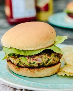 a burger with lettuce and tomato on a plate next to some potato chips