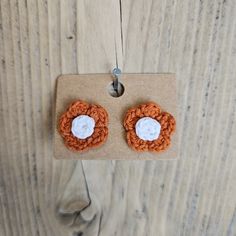 two orange crocheted flower earrings with white center on brown carded paper hanging from wood planks