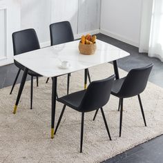 a white table with four black chairs and a bowl of fruit on top of it