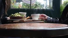 two people sitting at a table with plates and cups in front of them, one holding a coffee cup