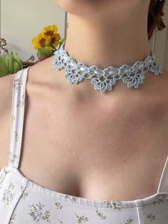 a woman wearing a blue crochet choker necklace with flowers in the background