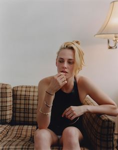 a woman sitting on a couch with her hand under her chin and looking at the camera