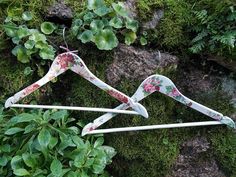 two clothes hangers sitting on top of a moss covered rock next to green plants