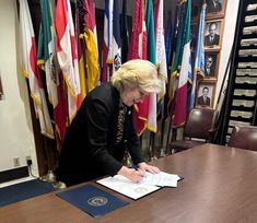 a woman sitting at a table signing papers in front of many flags and other items