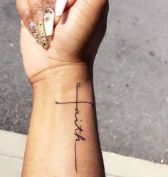 a woman's wrist with a cross and the word faith tattooed on her left arm