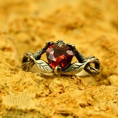 a red heart shaped ring sitting on top of a sandy surface with shells around it