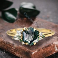 a green and white diamond ring sitting on top of a wooden block next to leaves