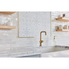 a white kitchen with gold faucet and marble counter tops on shelving above the sink