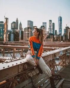 a woman sitting on top of a metal bench in front of a cityscape